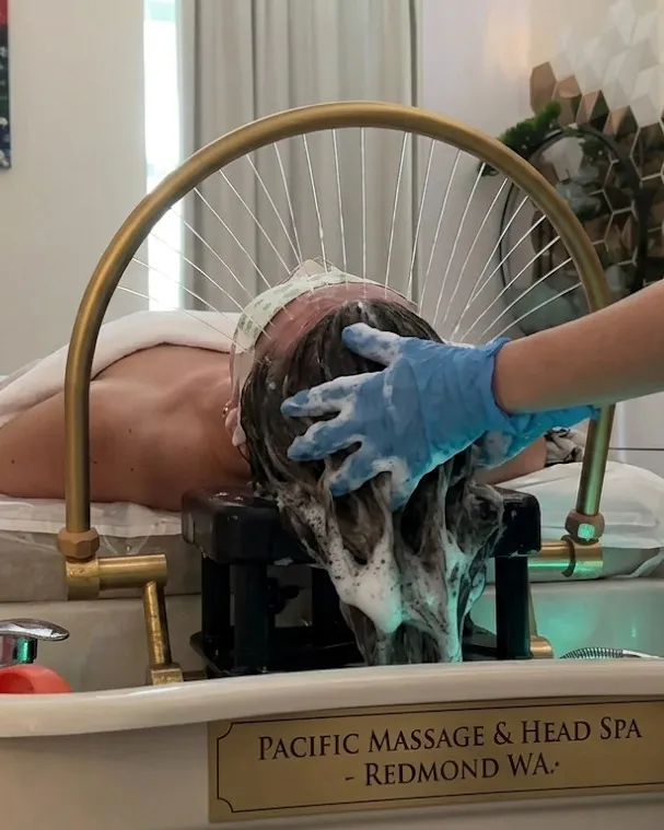 A guest reclined at the hydrotherapy basin with warm water running over the scalp during a head spa session